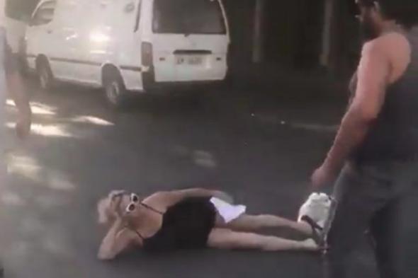 شاهد.. امرأة لبنانية تفترش الطريق بجسدها وتمنع مرور السيارات: “أنا هون بدي أقطع”